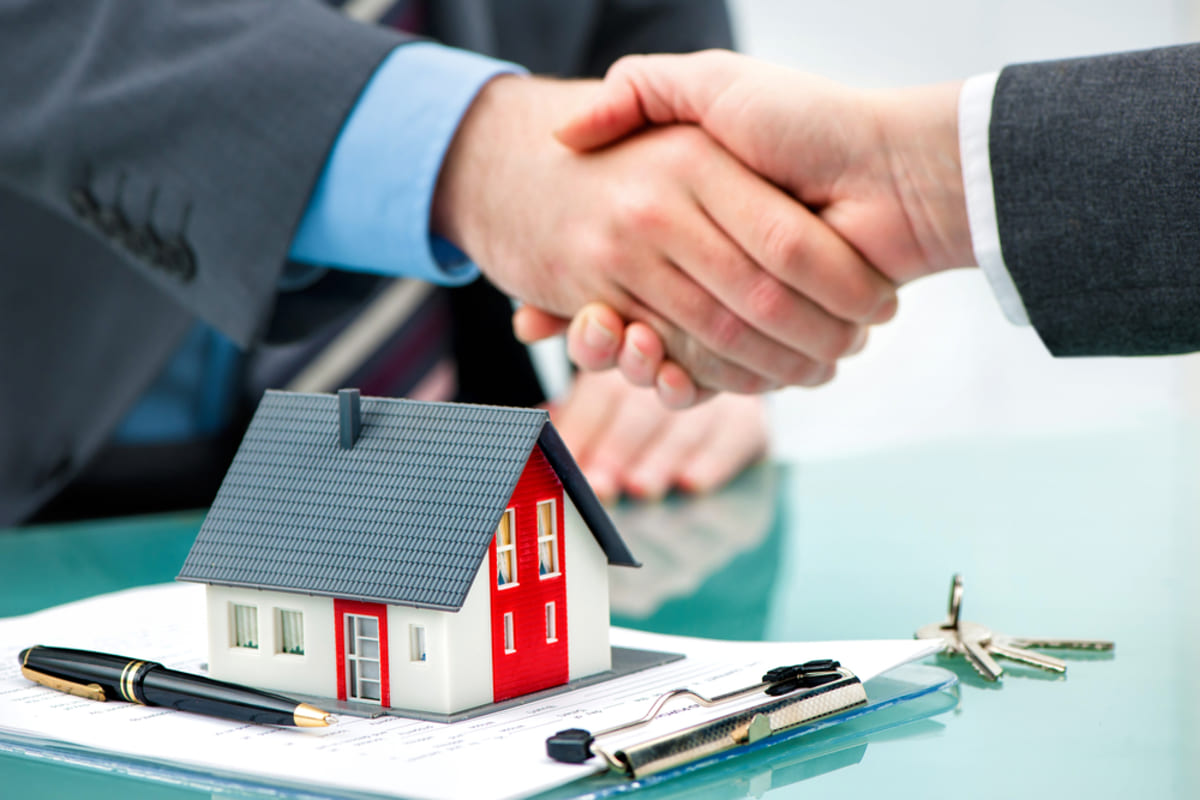 Close-up of hands shaking over a model house and contract, companies that buy houses for cash concept